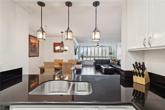 kitchen featuring dark countertops, crown molding, white cabinetry, pendant lighting, and a sink