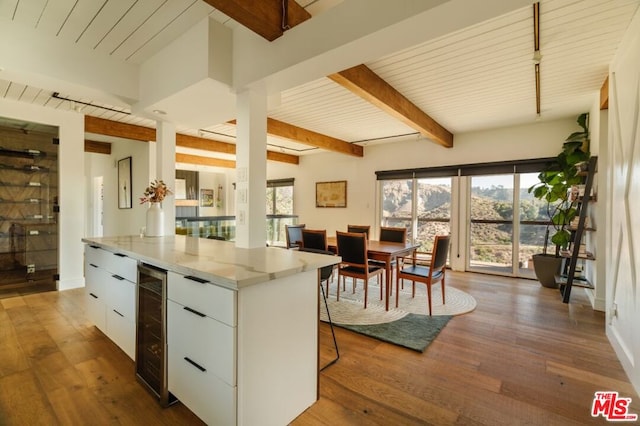 kitchen featuring light stone counters, dark wood-type flooring, beam ceiling, white cabinetry, and wine cooler