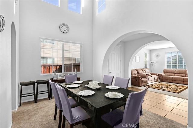 dining area featuring a wealth of natural light, a towering ceiling, and light colored carpet