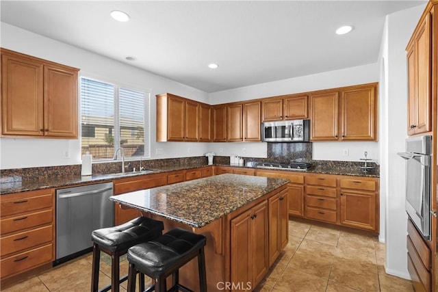 kitchen with dark stone counters, a breakfast bar, stainless steel appliances, sink, and a kitchen island