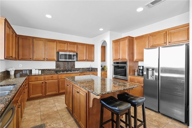 kitchen featuring a kitchen bar, a center island, dark stone counters, and appliances with stainless steel finishes