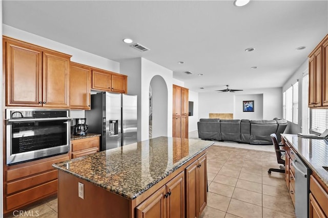 kitchen with ceiling fan, light tile patterned floors, dark stone counters, a kitchen island, and appliances with stainless steel finishes