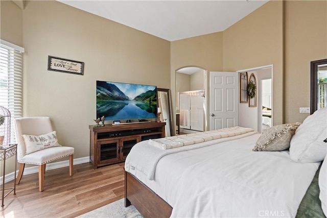 bedroom with connected bathroom, a high ceiling, and light wood-type flooring