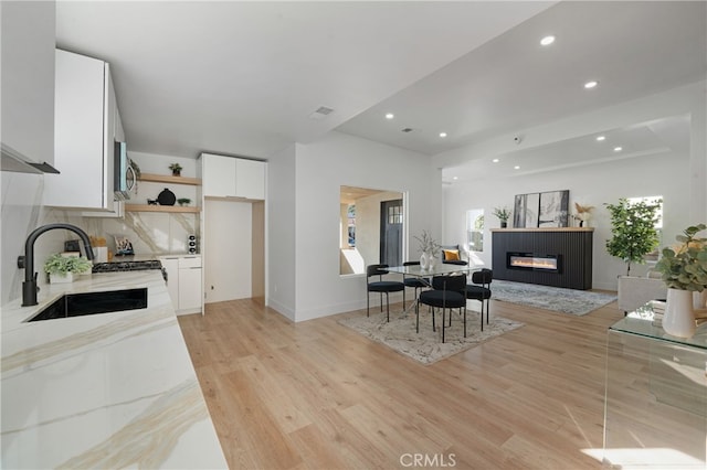 kitchen featuring sink, light hardwood / wood-style flooring, white cabinetry, tasteful backsplash, and light stone countertops