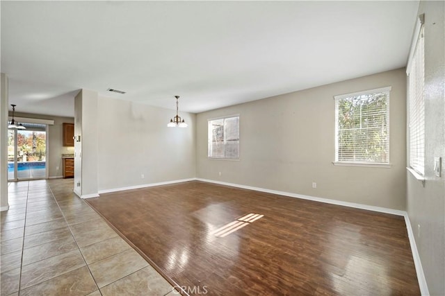 unfurnished room with a healthy amount of sunlight, tile patterned flooring, and a chandelier