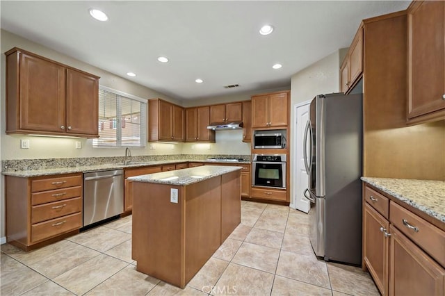 kitchen with appliances with stainless steel finishes, a center island, sink, light stone counters, and light tile patterned floors