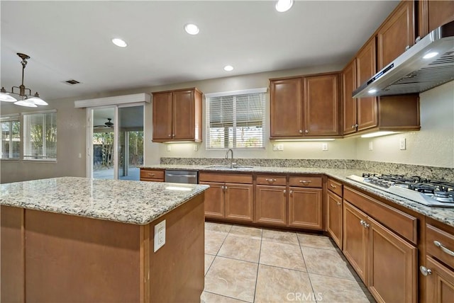 kitchen with stainless steel appliances, hanging light fixtures, light stone countertops, a kitchen island, and sink