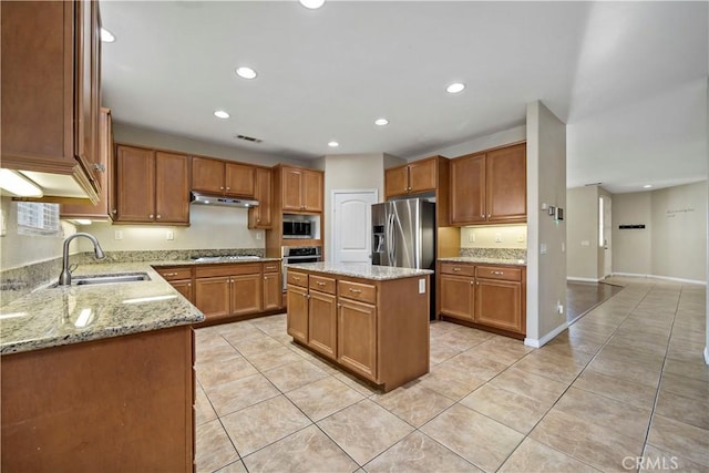 kitchen with light tile patterned floors, appliances with stainless steel finishes, light stone countertops, a kitchen island, and sink