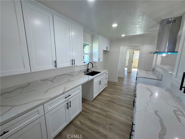 kitchen featuring exhaust hood, white cabinetry, sink, hardwood / wood-style flooring, and light stone counters