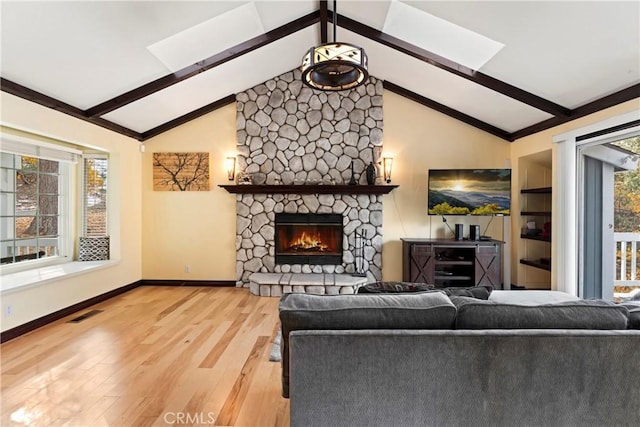 living room featuring hardwood / wood-style flooring, vaulted ceiling with beams, a stone fireplace, and a wealth of natural light