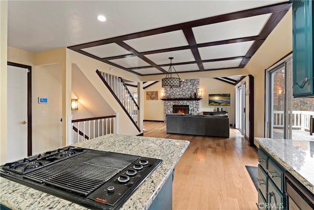 kitchen featuring coffered ceiling, a stone fireplace, light hardwood / wood-style flooring, black gas stovetop, and pendant lighting