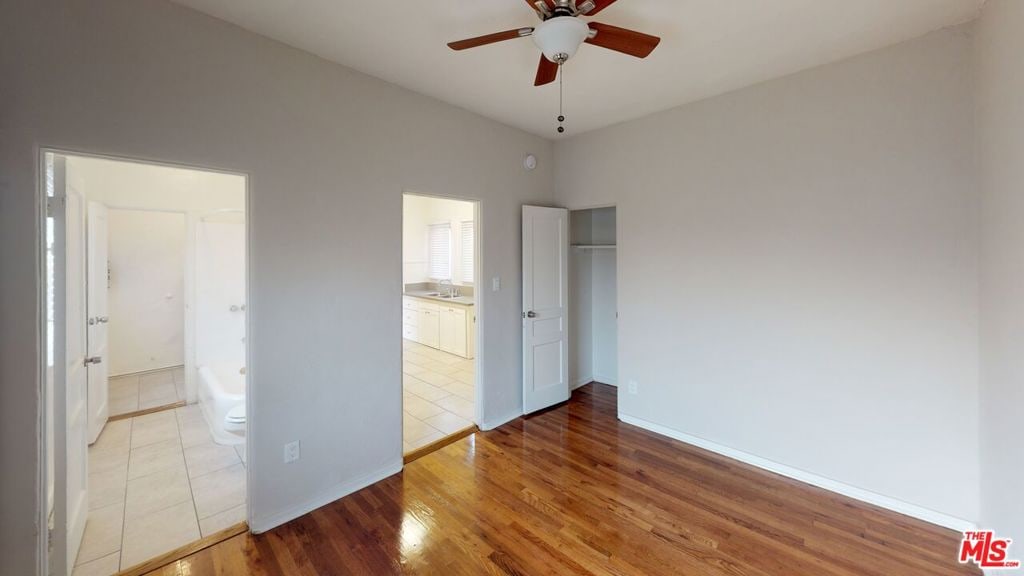 unfurnished bedroom featuring wood-type flooring, ensuite bath, and ceiling fan