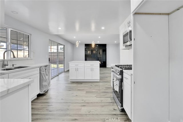 kitchen with sink, hanging light fixtures, light hardwood / wood-style flooring, white cabinetry, and stainless steel appliances