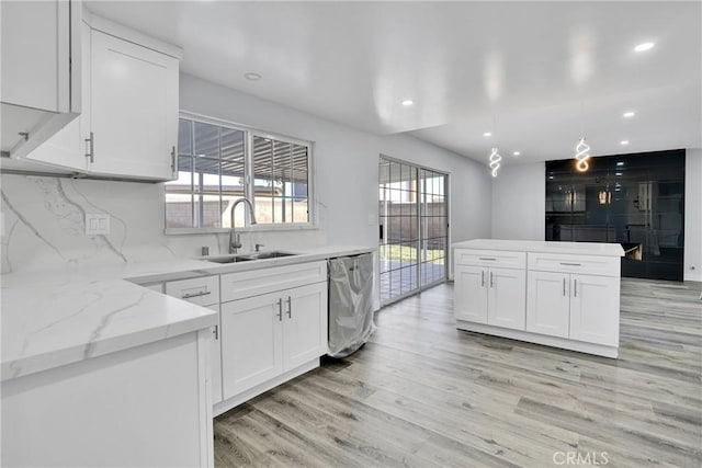 kitchen with white cabinets, sink, light hardwood / wood-style flooring, stainless steel dishwasher, and decorative light fixtures