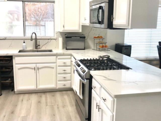 kitchen with backsplash, stainless steel appliances, sink, light hardwood / wood-style floors, and white cabinetry