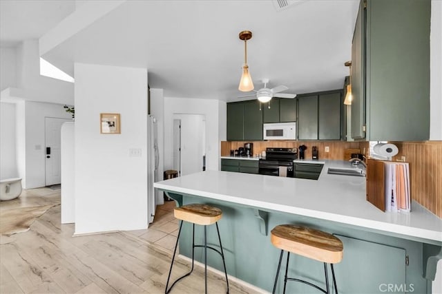 kitchen with a sink, light countertops, appliances with stainless steel finishes, a peninsula, and green cabinetry