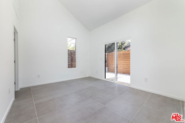 empty room with tile patterned floors, high vaulted ceiling, and plenty of natural light