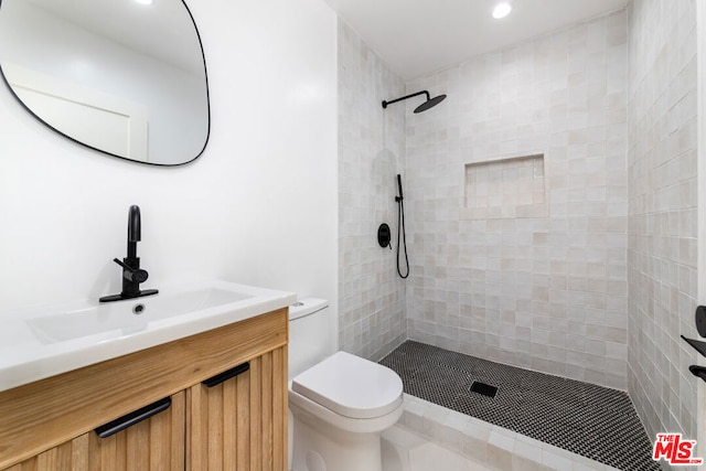 bathroom with tiled shower, vanity, and toilet