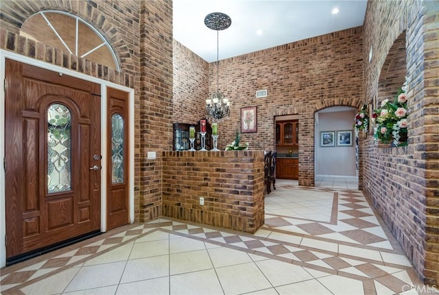 tiled entryway with brick wall, a high ceiling, and a notable chandelier