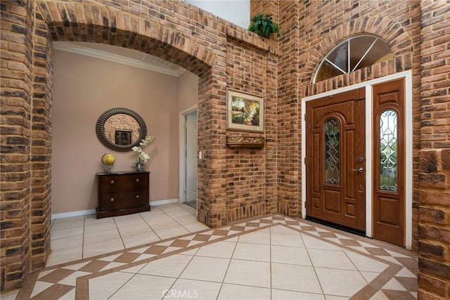 entrance foyer with brick wall, a towering ceiling, crown molding, and light tile patterned flooring