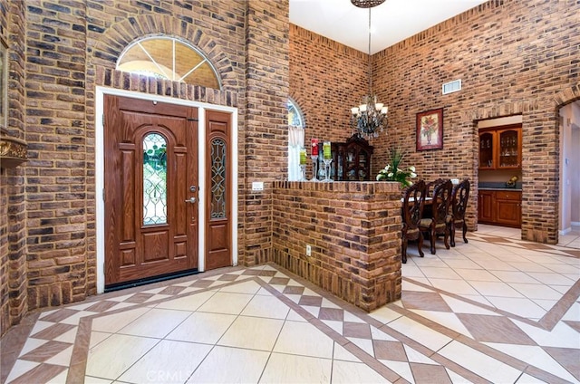 interior space with light tile patterned flooring, a towering ceiling, brick wall, and an inviting chandelier