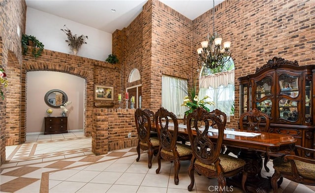 tiled dining area featuring a high ceiling, an inviting chandelier, and brick wall