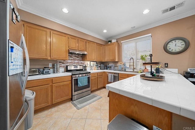 kitchen with ornamental molding, stainless steel appliances, sink, tile counters, and light tile patterned flooring