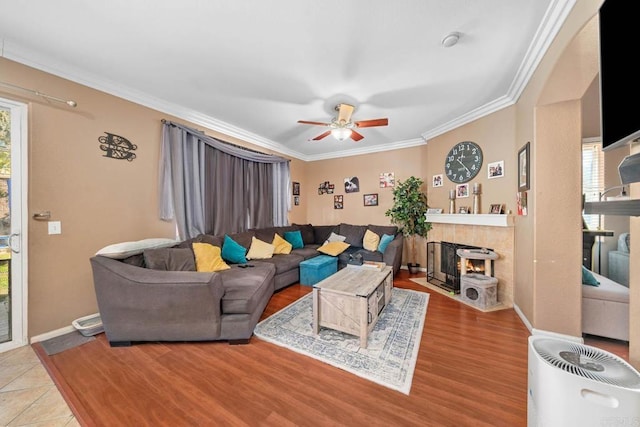 living room featuring ceiling fan, light hardwood / wood-style floors, crown molding, and a tile fireplace