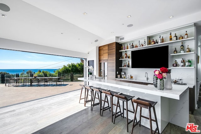 bar with sink, a water view, lofted ceiling, and hardwood / wood-style flooring