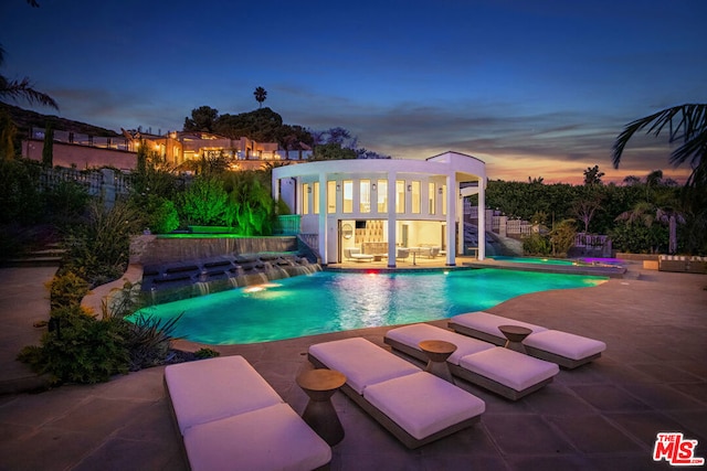 pool at dusk with a patio and pool water feature