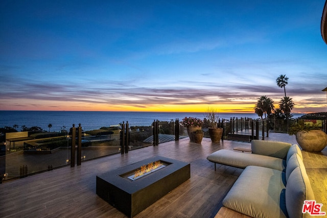 patio terrace at dusk featuring a water view and an outdoor living space with a fire pit