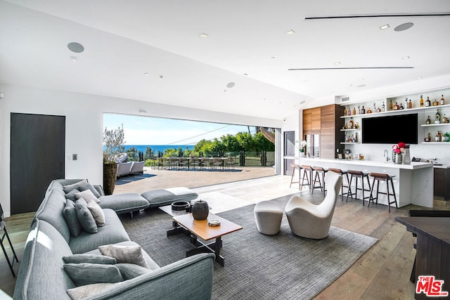 living room with indoor wet bar, lofted ceiling, and light wood-type flooring