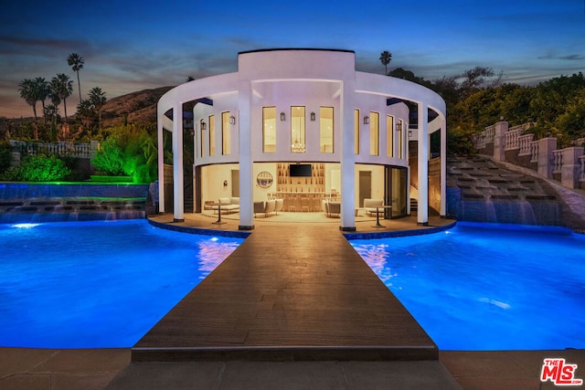 pool at dusk featuring pool water feature and a patio