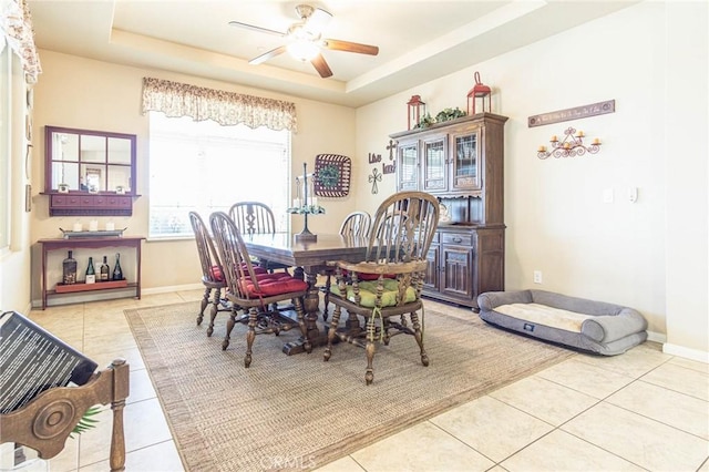 tiled dining space with ceiling fan and a tray ceiling