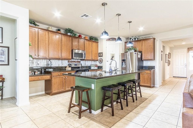 kitchen with sink, hanging light fixtures, stainless steel appliances, a kitchen bar, and a kitchen island with sink