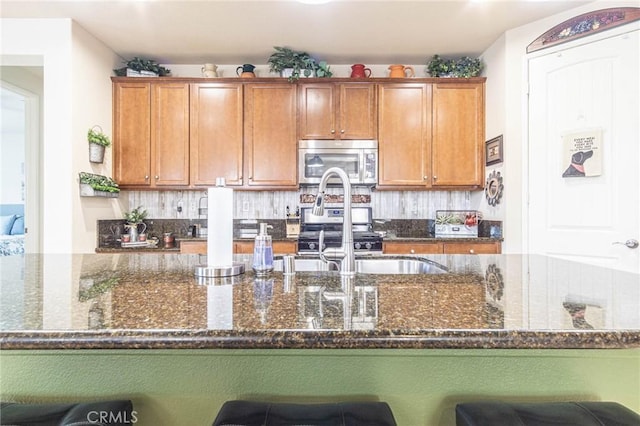 kitchen with dark stone countertops, a kitchen bar, sink, and appliances with stainless steel finishes