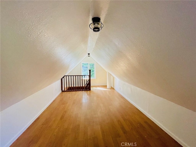 bonus room with vaulted ceiling, a textured ceiling, baseboards, and wood finished floors