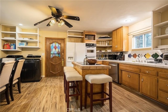 kitchen featuring tile countertops, a breakfast bar, white appliances, and light hardwood / wood-style flooring