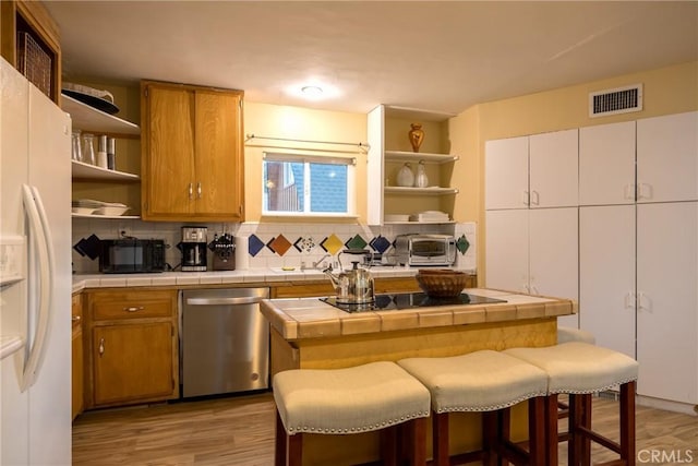 kitchen featuring light wood-type flooring, stainless steel dishwasher, black electric cooktop, white refrigerator with ice dispenser, and tile counters