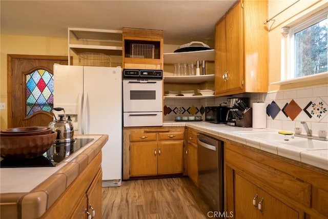 kitchen with tile countertops, stainless steel dishwasher, tasteful backsplash, and light hardwood / wood-style flooring