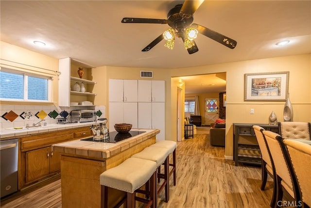 kitchen with decorative backsplash, stainless steel dishwasher, sink, light hardwood / wood-style flooring, and tile counters