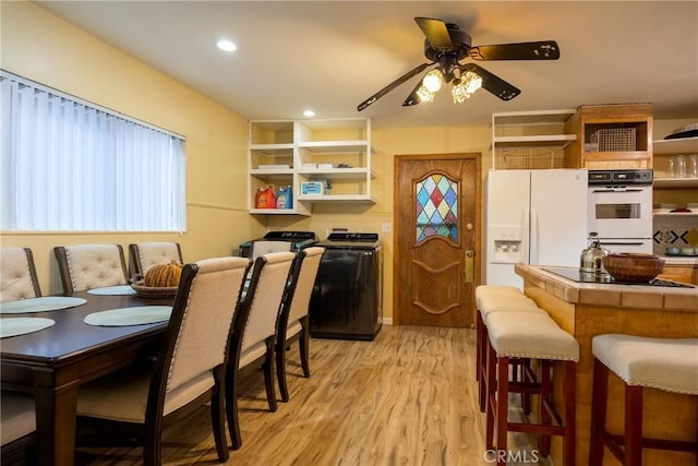 kitchen featuring a kitchen breakfast bar, white appliances, ceiling fan, washer / dryer, and light hardwood / wood-style floors