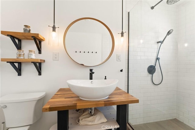 bathroom with tiled shower, toilet, and sink