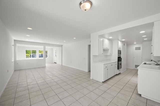 kitchen with stainless steel microwave, sink, light tile patterned floors, black oven, and white cabinetry