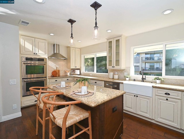 kitchen featuring appliances with stainless steel finishes, dark hardwood / wood-style flooring, wall chimney exhaust hood, sink, and a kitchen island