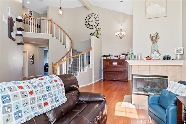 living room with hardwood / wood-style floors, high vaulted ceiling, an inviting chandelier, beamed ceiling, and a tiled fireplace