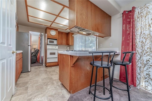 kitchen with ventilation hood, a breakfast bar, white appliances, and kitchen peninsula