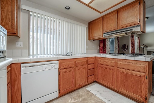 kitchen featuring tile countertops, dishwasher, kitchen peninsula, and exhaust hood