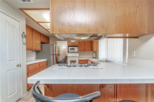 kitchen featuring kitchen peninsula, tile counters, sink, and white appliances