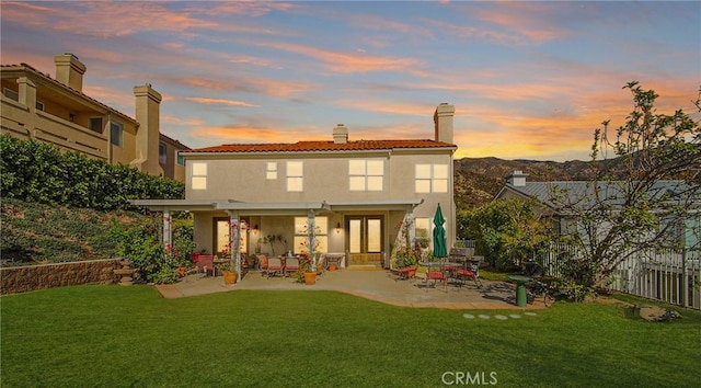 back house at dusk with a yard and a patio